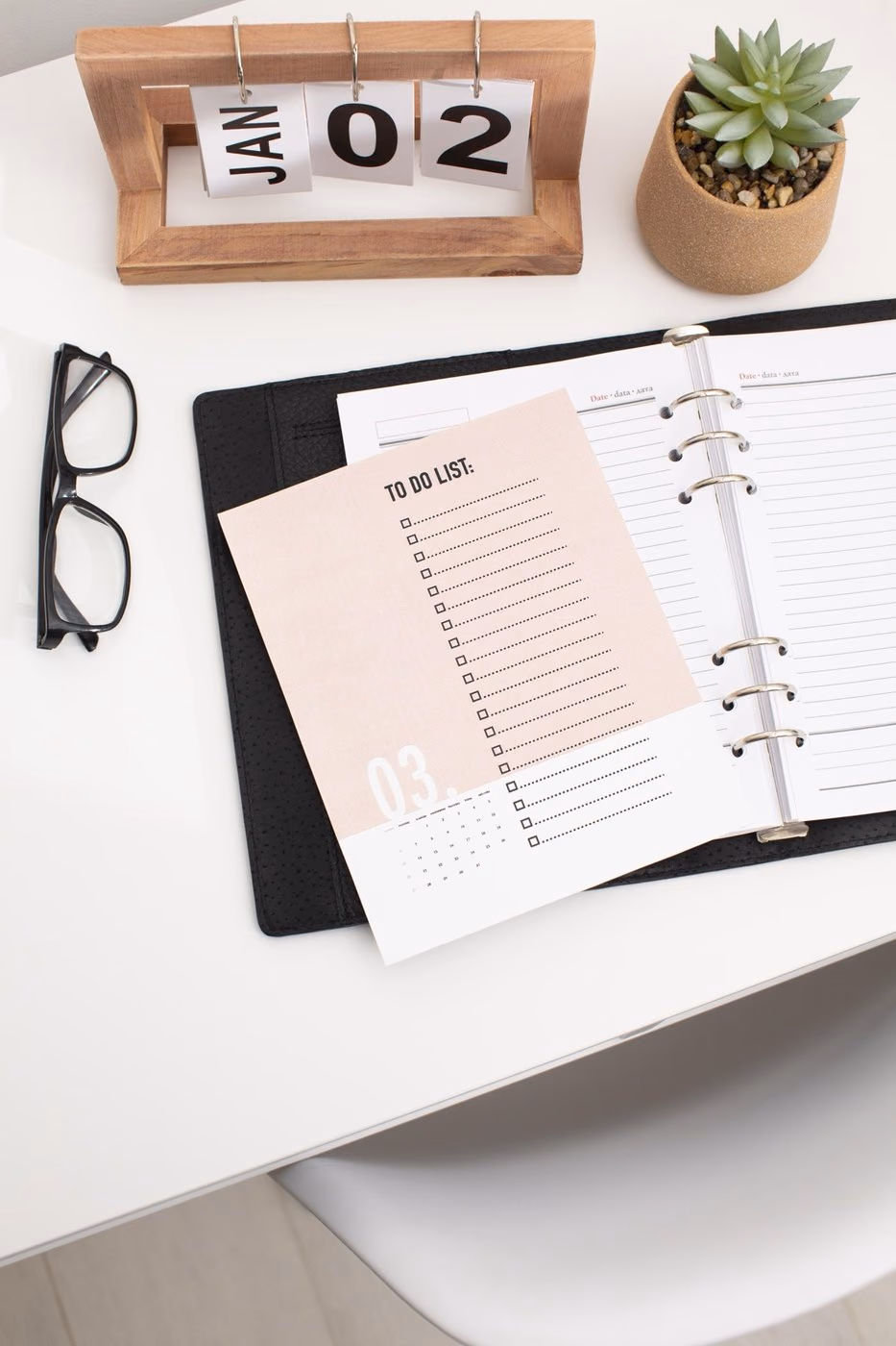 Un planner d'objectifs ouvert sur un bureau, à côté de lunettes et d'un carnet